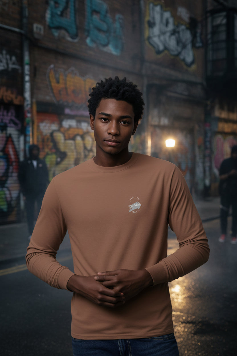 Urban Artistic Threads Signature Logo Long Sleeve Tee in tan with white chest logo, worn by man in graffiti alley.