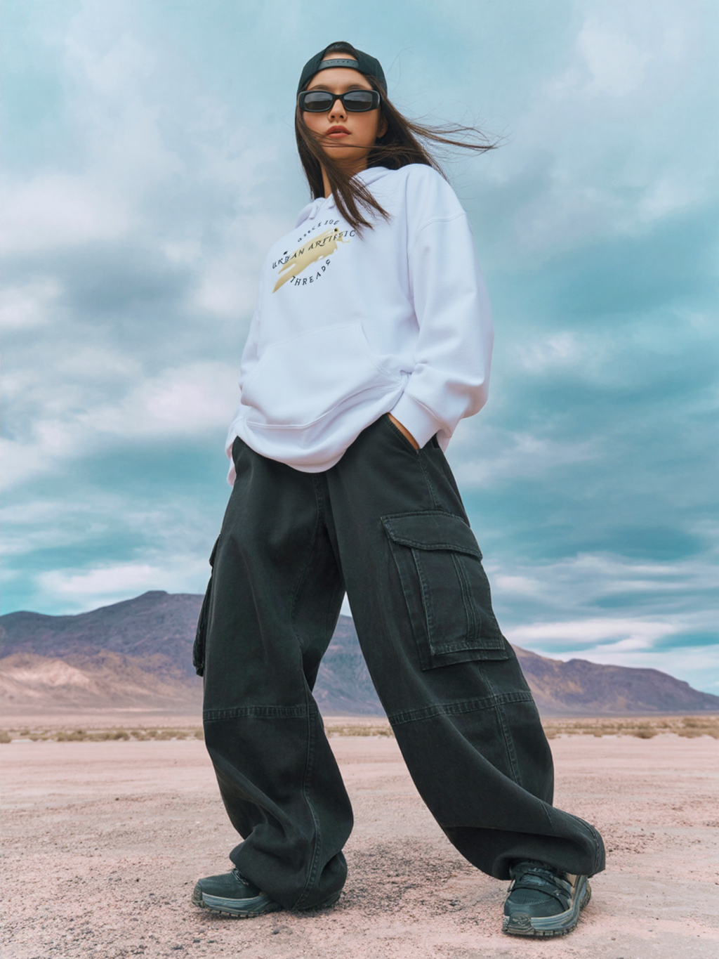 Model wearing Urban Artistic Threads Hoodie in white with cargo pants, desert backdrop and city-life streetwear vibe.