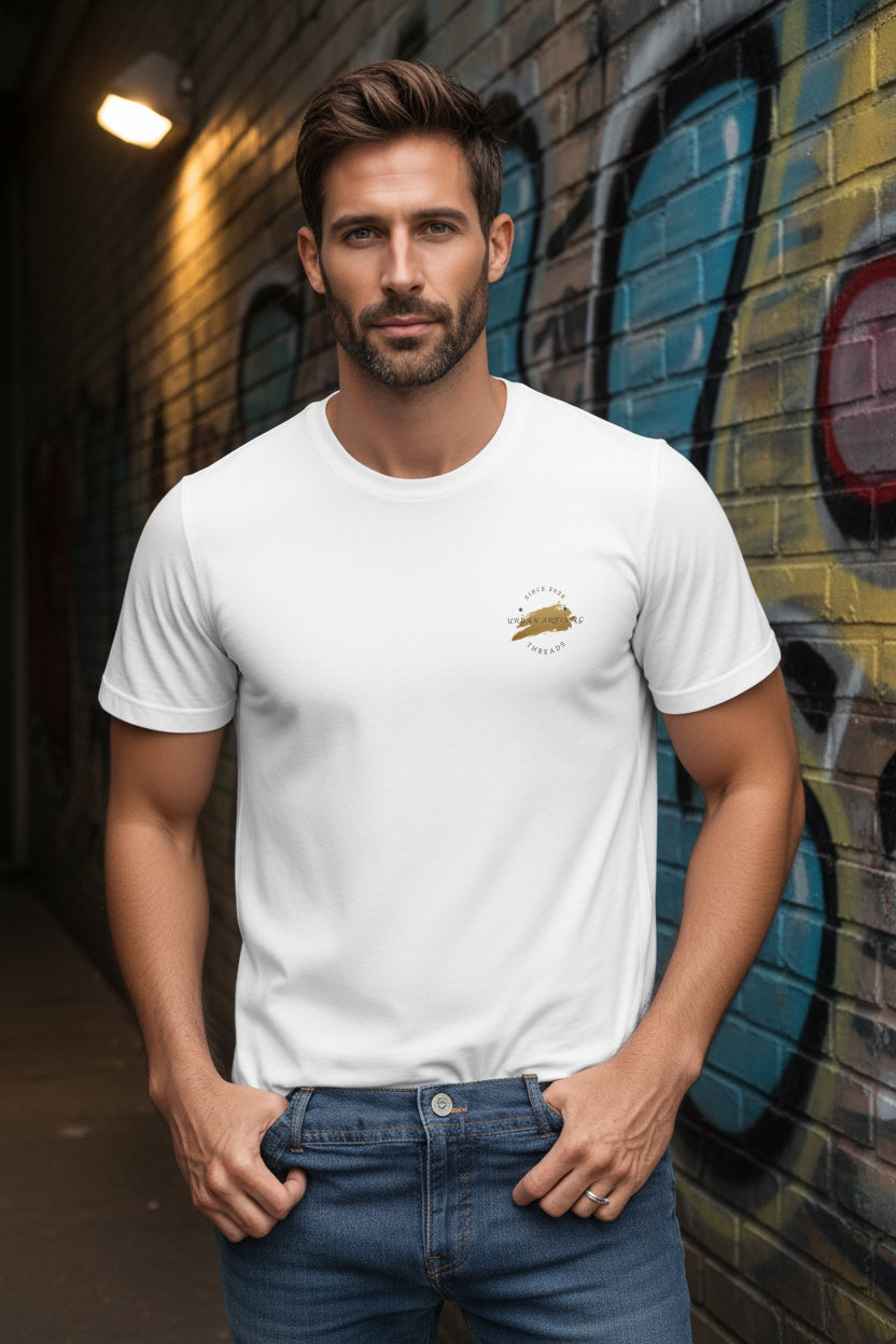 Male model wearing Urban Artistic Signature Logo Tee with a gold paint-stroke emblem on the chest, graffiti wall.